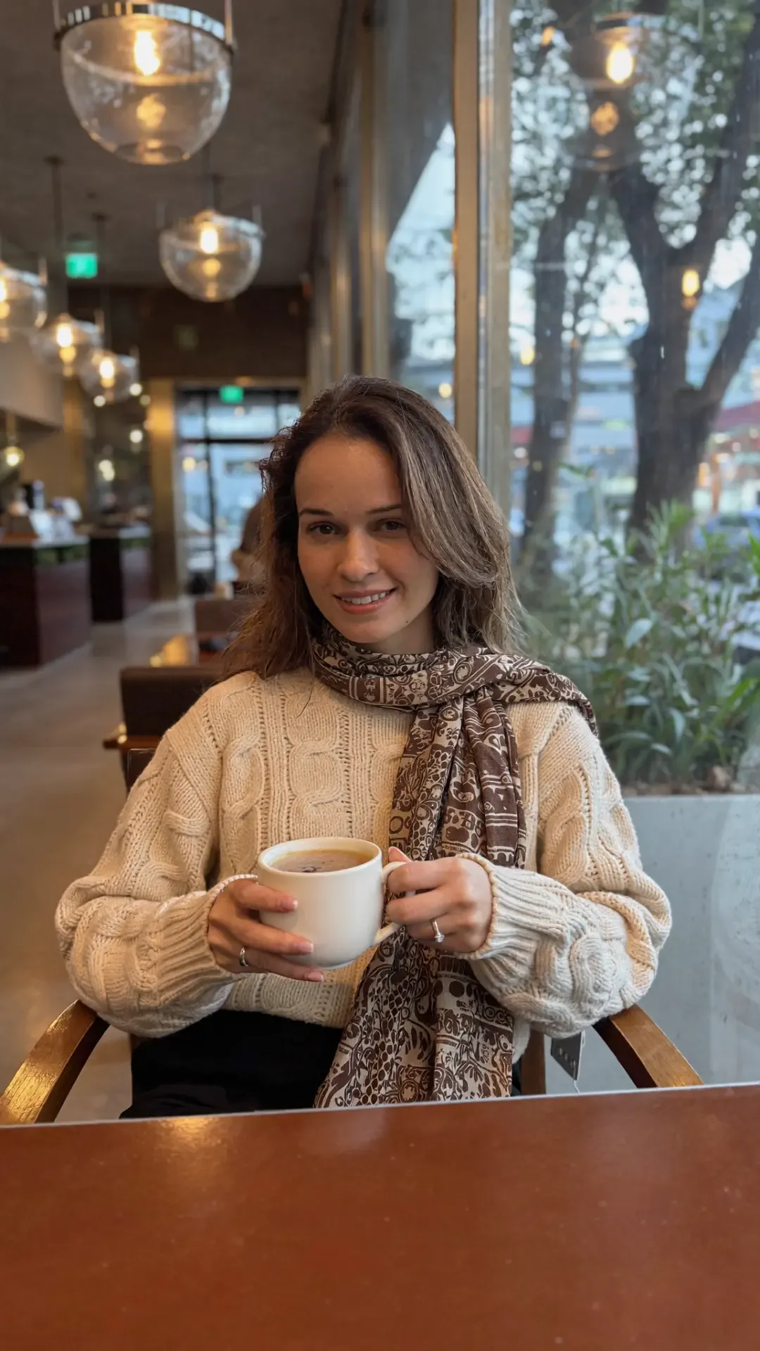Komel Kaur, psychotherapist, sitting with a coffee by a cafe window